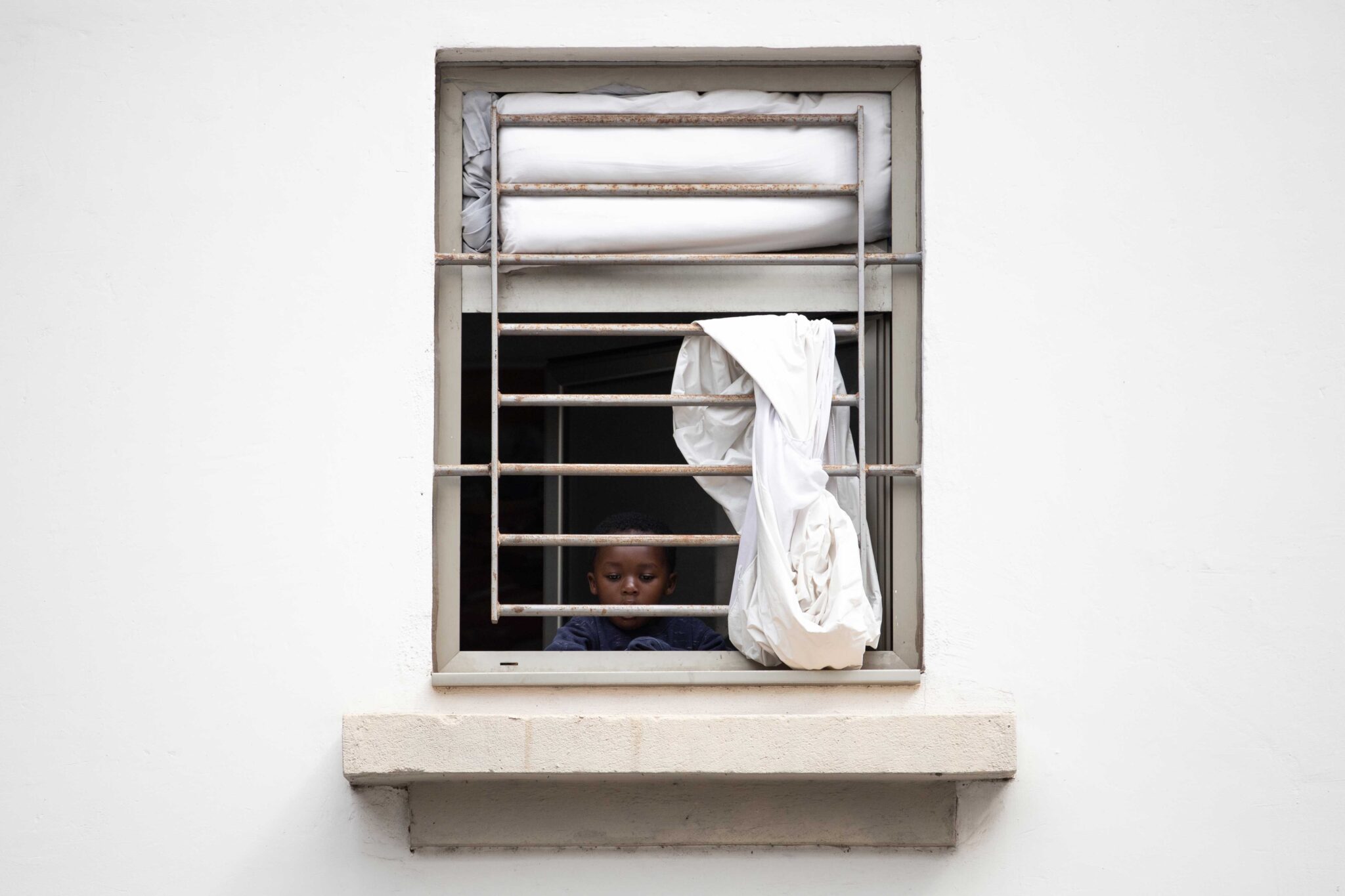 Un nen mira per la finestra de la seva habitació a l’antiga presó de Tenerife, ara convertida en centre per a persones migrants. En aquest centre només hi ha infants i dones. Santa Cruz, Tenerife.