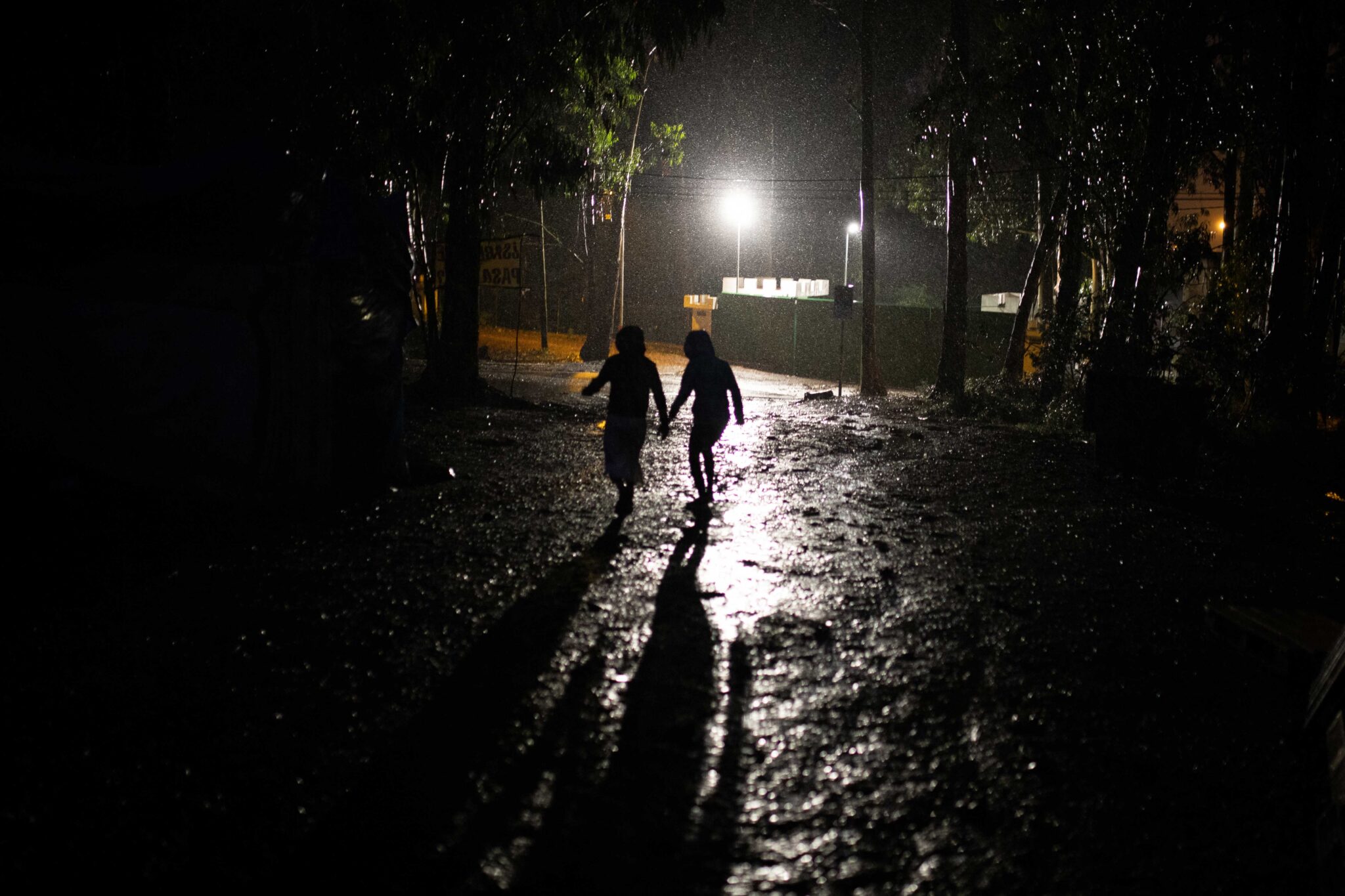 Dos persones migrants corren a resguardar-se de la tempesta davant de la porta del campament de ‘Las Raíces’. La Laguna, Tenerife.